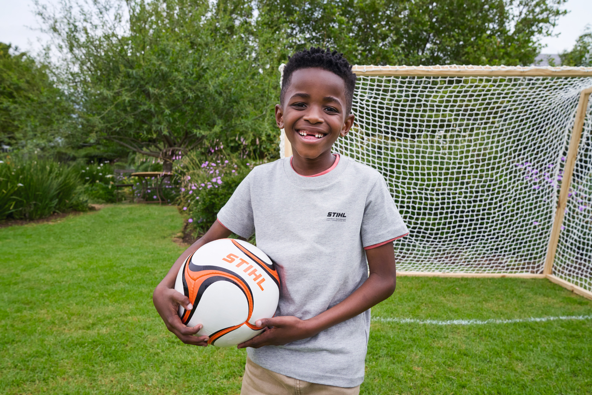 Un garçon tout sourire tient un ballon de football STIHL dans la main devant le nouveau but 