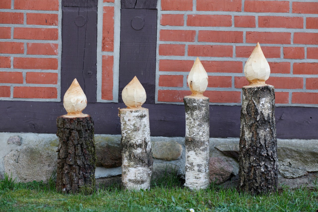 Quatre bougies en bois sur une pelouse devant un mur de briques rouges