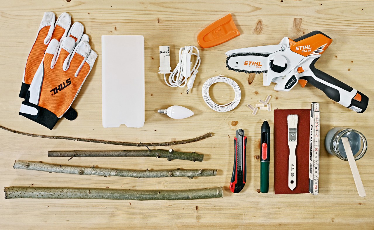 Matériel pour créer une table de salon en brindilles : gants, scie de jardin STIHL GTA 26, branches, entre autres