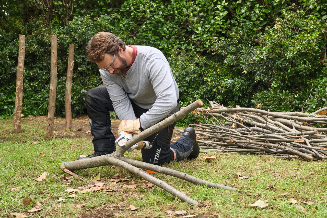 Homme coupant de grosses branches à la longueur souhaitée avec une scie de jardin STIHL GTA 26