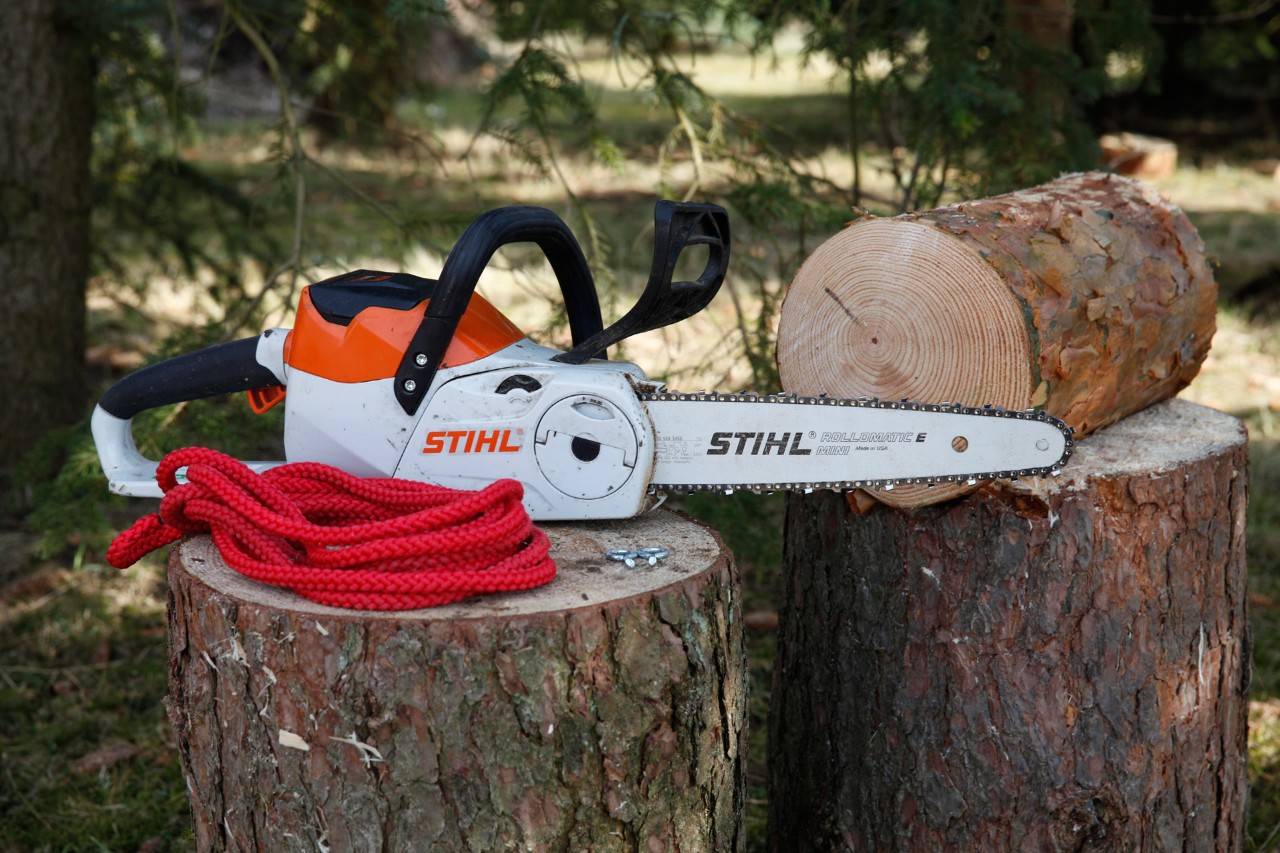 Faire une mangeoire à oiseaux : une tronçonneuse STIHL MSA 140 C, deux boulons à œil et corde rouge posés sur un tronc