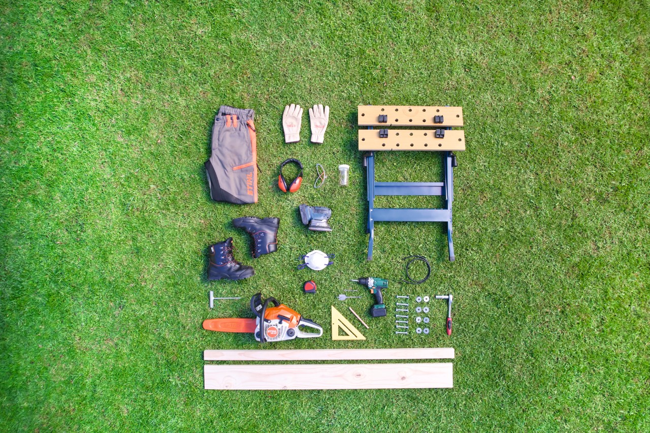 Les outils et le matériel sont disposés en carré sur une pelouse en vue de la fabrication d’un chevalet de sciage 