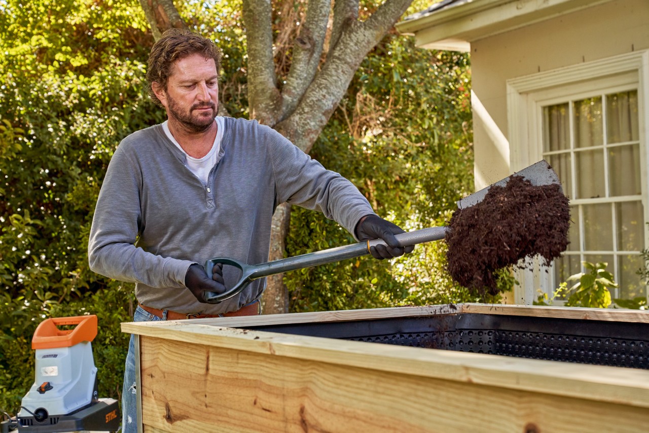 Un homme muni d’une pelle remplit un potager surélevé de compost semi-transformé