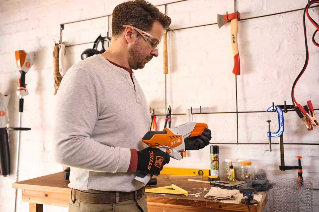 Un homme portant des lunettes de protection retire le capuchon de protection de la scie de jardin à batterie STIHL GTA 26