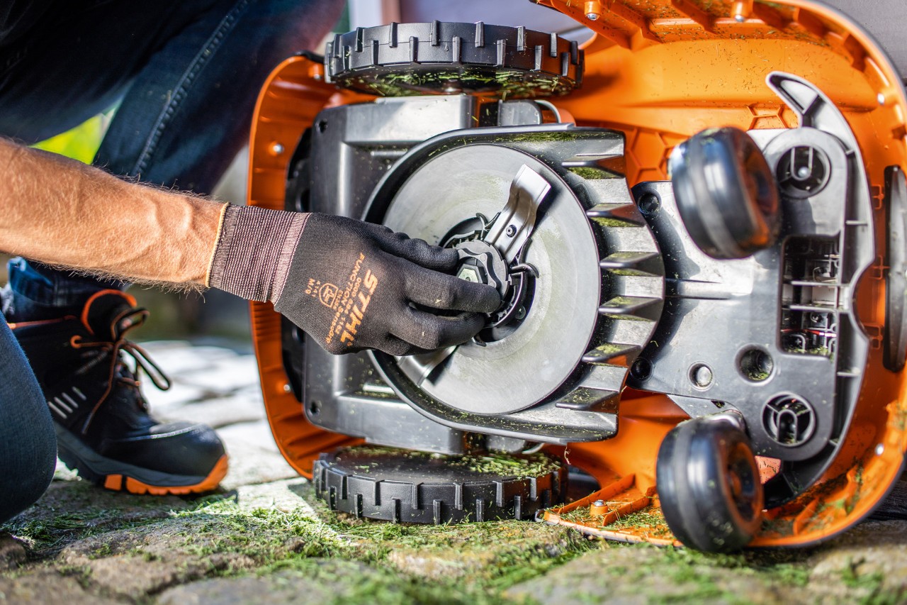 Un robot de tonte STIHL iMOW® RMI 422 mis sur le côté pendant qu’une personne portant des gants vérifie la lame