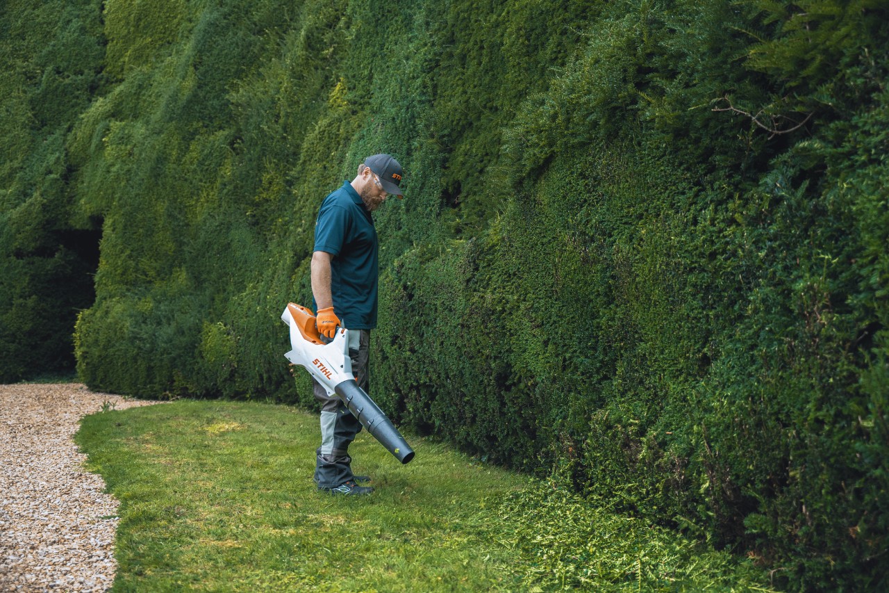 Een professional staat met een STIHL accubladblazer voor de hoge heg van het Bathurst Estate