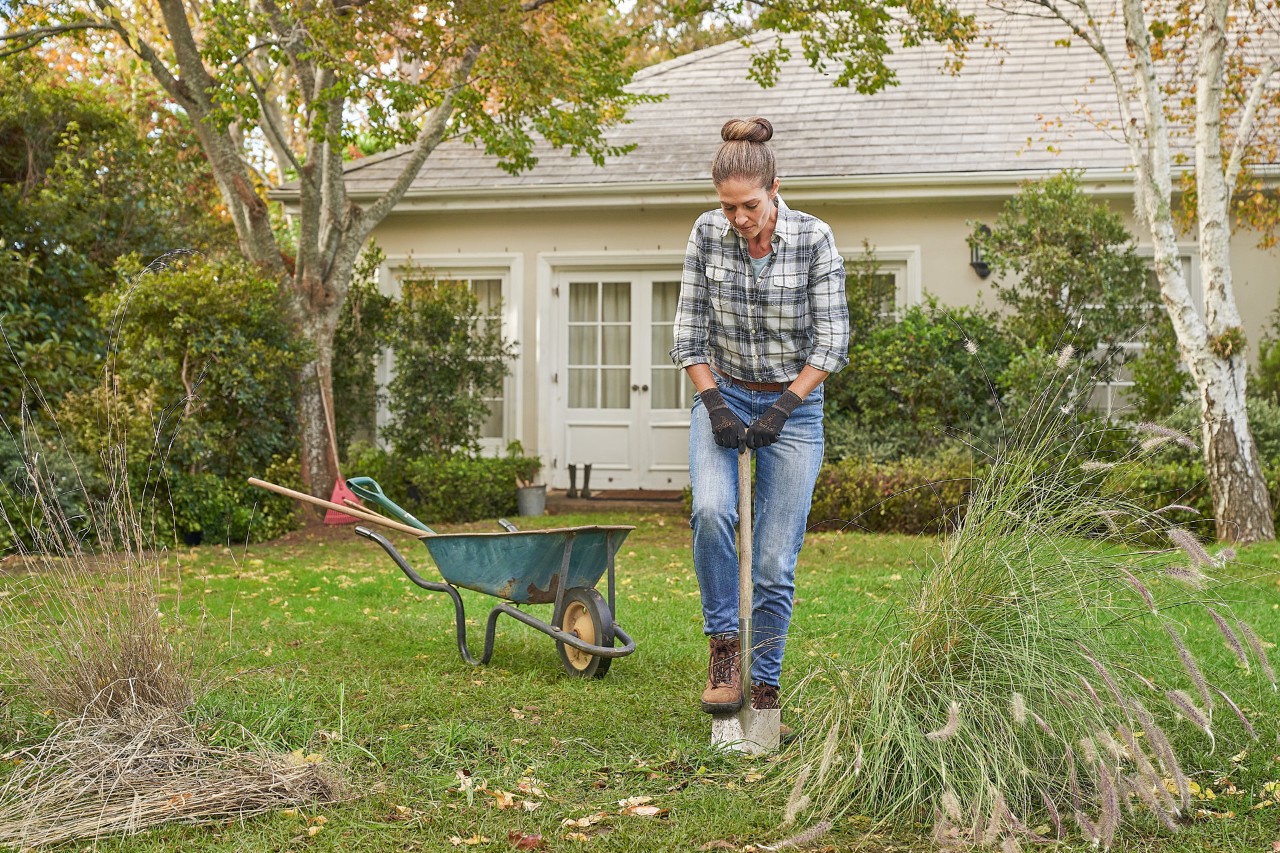 Een vrouw met STIHL Function SensoTouch veiligheidshandschoenen werkt met een spade in de tuin om een heg te planten